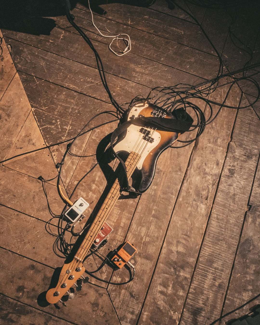 A bass guitar and a tangle of cables lying on a wooden stage floor before load-in